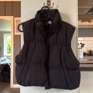 Svart väst från H&M - Snygg svart väst från H&Mmed hög krage och dragkedja framtill. Västen har en puffig, quiltad design och två stora fickor på sidorna. Perfekt att slänga över en hoodie för en cool look.