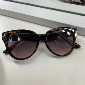 Leopardmönstrade solglasögon från Zign - Snygga solglasögon från Zign med leopardmönstrad båge i brunt och svart. Cat-eye formade glas med mörka tonade linser. Perfekt accessoar för att lyfta din stil med en trendig touch.