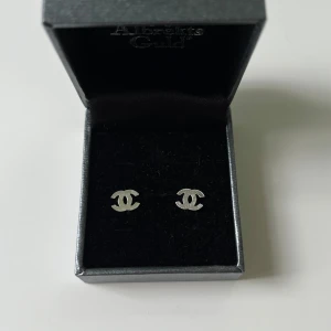 Silver örhängen  - Snygga örhängen i äkta silver och helt nytt skick, som liknar Chanel i klassisk CC-logga. De är i silverfärg och har en stilren, minimalistisk design som verkligen poppar. Perfekta för dig som vill ha en ikonisk accessoar med lyxig känsla.