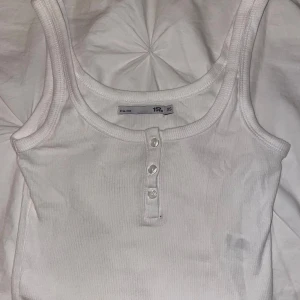 Vit ribbad linnetopp från lager 157  - Säljer en vit ribbad linnetopp från lager 157 i storlek XS. Toppen har rund halsringning och tre knappar framtill som snygg detalj endast använd ett fåtal gånger!🥰
