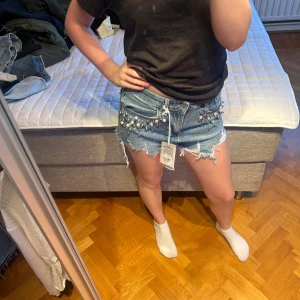 Blå jeansshorts med pärlor  - Ljusblåa jeans med pärl detaljer. Lågmidjade och passar S/M. Aldrig använda och har prislappen kvar.
