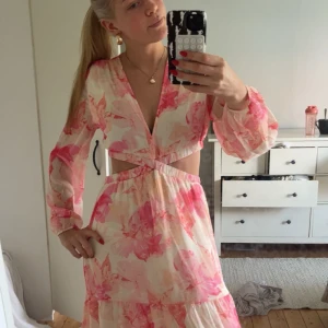 Blommig långklänning med cut-outs - Superfin långklänning med blommigt mönster i rosa och ljusa toner. Klänningen har v-ringning, långa ärmar och snygga cut-outs i midjan. Materialet känns lätt och flowy, perfekt för sommarens alla tillfällen. Volangdetaljer på kjolen ger extra rörelse. Andvänd en gång den är i super bra skick, storlek 36💞