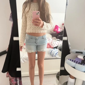 Ljusblå jeansshorts med spetsdetalj - Säljer ett par ljusblå jeansshorts med snygga spetsdetaljer i vitt längs bensluten. Shortsen har normal passform, klassiska fickor fram och bak samt råa kanter för en chill vibe. Perfekta för sommaren och lätta att matcha med allt.