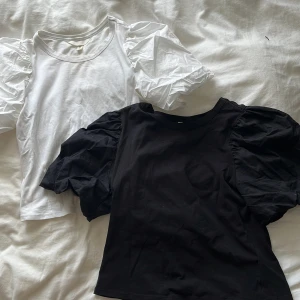 2 puffärmade toppar från H&M - Två snygga toppar från H&M, en i vitt och en i svart. Båda har puffiga korta ärmar och rund halsringning. Tillverkade i mjuk bomull, perfekta för att ge outfiten en trendig touch. Säljes tillsammans!