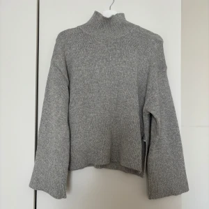 Grå polotröja från Gina Tricot - Mysig grå polotröja från Gina Tricot i stickat material. Tröjan har hög krage, långa ärmar och en loose fit med ribbade detaljer vid ärmslut och nederkant. Perfekt för lager-på-lager och chill höst- och vinterstil.