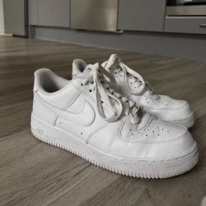 Nike Air Force 1 vita sneakers strl 43 - Klassiska Nike Air Force 1 i helvitt skinn med perforerad tå, rund tå och platt sula. Snygg och tidlös modell med snörning och diskret silverdetalj vid snörningen. Perfekta för dig som gillar clean och stilren streetwear. Storlek 43
