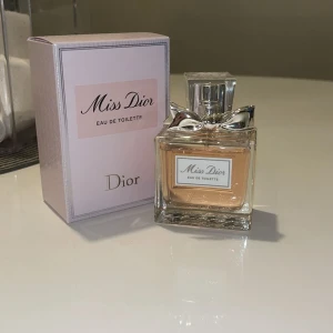 Miss Dior Eau de Toilette 50ml - Miss Dior Eau de Toilette från Dior i en elegant fyrkantig glasflaska med silverfärgad rosett och transparent lock. Parfymen är ljusrosa och kommer i en stilren ljusrosa kartong. Flaskan rymmer 50 ml och utstrålar lyxig och feminin känsla.