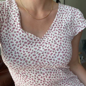 Vit blommig midiklänning  - Supersöt midiklänning i vitt med små rosa och beige blommor. Klänningen har v-ringning, korta ärmar och en figurnära passform. Luftigt och skönt material. 