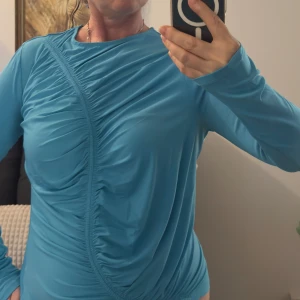 Turkos långärmad topp från C.W. - Snygg turkos långärmad topp från C.W. med cool rynkad detalj framtill som ger en unik look. Tillverkad i ett mjukt och stretchigt syntetmaterial som sitter skönt på kroppen. Oanvänd dock har jag hunnit klippa av etiketten på insidan.