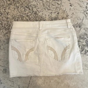 Vit jeanskjol från Hollister - Stretchig i materialet. Vit jeanskjol från Hollister med fem fickor och snygga detaljer på bakfickorna. Kjolen har knappar framtill och rå kant nertill för en cool look. Perfekt för dig som gillar en klassisk men trendig stil.