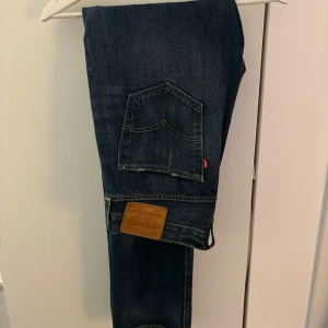 Levi's 501 mörkblå jeans straight fit - Klassiska Levi's 501 jeans i mörkblå tvätt med raka ben och snygga slitningar vid benslut. Riktig snygg tvätt. Storlek 32/34.