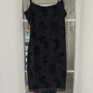 Svart klänning med tigerprint H&M Divided - Svart kortklänning från H&M Divided med tunna axelband och sammetsmönster av tigrar över hela tyget. Klänningen har en rak passform och lätt vågig kant nertill. Jättefin passform!