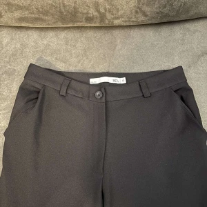 Svarta kostymbyxor XS - Svarta kostymbyxor från 157 i klassisk rak modell med hällor för bälte och diskreta sidfickor. Snyggt skräddade och perfekta för en clean och stilren look. Materialet känns mjukt och följsamt.