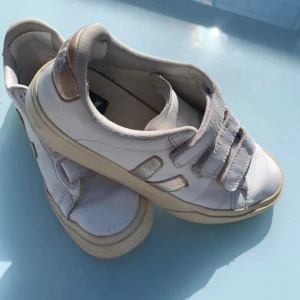 Vita Veja sneakers med kardborre - Snygga vita sneakers från Veja med klassisk design och tre kardborreband. Skorna har beige detaljer och rund tå. Tillverkade i skinn med bekväm platt sula. Perfekta för en clean och stilren look. Nypris 1920kr