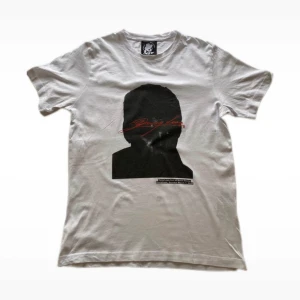 Yung Lean Stockholm 2025 Merch - Vit t-shirt från World Affairs med svart siluett-tryck och röd text på bröstet. Klassisk passform med rund hals och korta ärmar. Mjuk bomullskvalitet som känns skön mot huden. Perfekt för dig som gillar streetwear och unika prints.