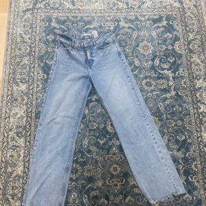 Ljusblå raka jeans från Zara - Ljusblå jeans från Zara med rak passform och hög midja. Jeansen har klassisk femficksdesign, dragkedja och knapp framtill samt råa, fransiga benslut för en avslappnad vibe. Tillverkade i bomullsdenim.