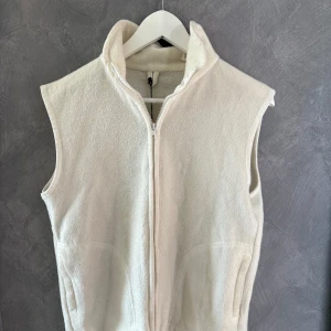 Vit fleeceväst från Yves Rocher - Säljer en vit fleeceväst från Yves Rocher i storlek L. Västen har hög krage, hel dragkedja framtill och två fickor på sidorna. Perfekt för lager-på-lager och enkel att matcha med andra plagg. Stilren och clean look. (Obs liten i storleken)