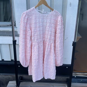 Ljusrosa kort klänning Gina Tricot - Supersöt ljusrosa kort klänning från Gina Tricot med strukturerat rutigt tyg, långa ärmar och öppen rygg med knytband. Klänningen har en voluminös passform och rund halsringning framtill. Perfekt för dig som gillar romantisk och trendig stil. Helt nya på grund av att dom inte passade