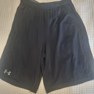 Svarta shorts Under Armour - Svarta träningsshorts från Under Armour med fickor, elastisk midja och logga på vänster ben. Klassisk passform. Se bilder för mått. Se gärna även mina andra annonser.