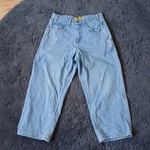 Baggy jeans från Butter goods, ljusblå, strl 28 - Baggy ljusblå jeans från Butter goods med riktigt loose fit och broderad detalj på fickan. Klassisk femficksmodell i jeansmaterial, med coolt broderi både fram och bak. Perfekta för dig som gillar streetwear och oversized stil.
