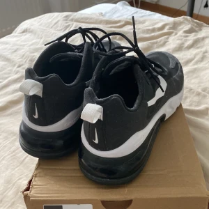 Nike React Sneakers - Svarta och vita Nike React sneakers med snygg, sportig design och tydlig Swoosh-logga på sidan. Skorna har snörning, rund tå och en bekväm, dämpad sula. Perfekta för dig som gillar streetwear och vill ha en stilren look.