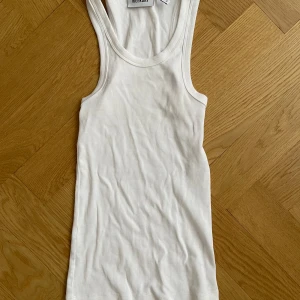 Vit ribbad linnetopp linne från Weekday - Säljer en klassisk vit ribbad linnetopp från Weekday i storlek XS. Toppen har en tight passform, är ärmlös och har rundad halsringning. Perfekt för lager-på-lager eller att bära som den är under varma dagar. Aldrig använd.