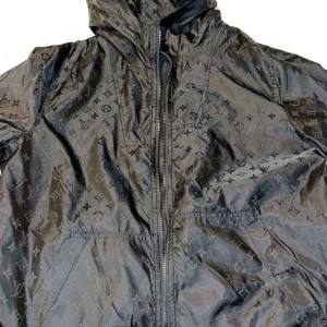 Svart Louis Vuitton vindjacka med monogram - Snygg svart vindjacka från Louis Vuitton med ikoniskt monogrammönster över hela jackan. Jackan har huva, dragkedja framtill och praktiska fickor. Materialet är glansigt och lätt, perfekt för en streetstyle-look.