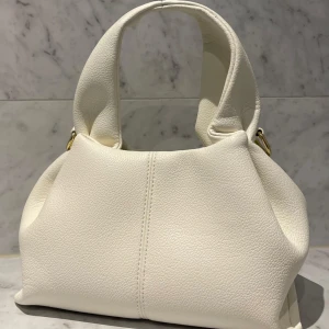 Vit handväska med gulddetaljer - Superfin väska som jag köpte på plick, använt fåtal gånger men den kommer tyvärr inte till användning mera💕väskan var helt oanvänd när jag köpte den så den är i mycket bra skick!