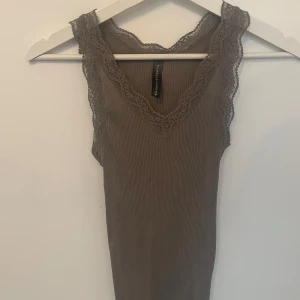 Ribbad brun linnetopp med spets - Supersnygg brun ribbad linnetopp från bombyx & sindon med v-ringad hals och breda spetskantade axelband. Toppen är ärmlös och har en slim passform som sitter riktigt snyggt. Perfekt att styla med jeans eller kjol för en chill look.strl s. Använd 1 gång. Går att pruta 