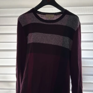 Randig vinröd tröja från Burberry - Snygg vinröd och mörkgrå randig tröja från Burberry i storlek M. Tröjan har rund hals och långa ärmar, med breda horisontella ränder i olika nyanser av vinrött och grått. Perfekt för dig som gillar klassisk stil med en modern twist. Otroligt snygg pris ej hugget i sten 