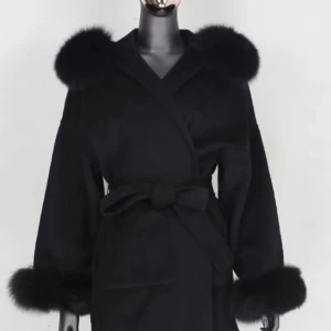 Svart kappa med fuskpälsdetaljer - Snygg svart kappa med päls på ärmslut som går att ta av och sätta på med knappar och luvan. Jackan har bälte i midjan för en schysst siluett och är perfekt för dig som vill ha en elegant och trendig look. Passar till alla outfits när det är kallt ute. Den har 2 fickor längst fram, man kan ha den med skärpet stängt eller öppet både och ser jätte fint ut.