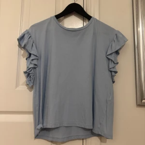 Ljusblå volangtopp från Zara - Supersöt ljusblå topp från Zara med volangdetaljer på ärmarna. T-shirtdesign med rund halsringning och korta ärmar.