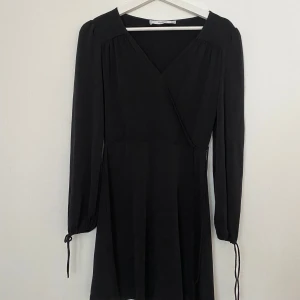 Svart omlottklänning från Mango XS - Supersnygg svart kortklänning från Mango Basics i omlottmodell med v-ringning och långa ärmar med knyt vid ärmslut. Stilren och enkel design som passar perfekt till dig som gillar minimalistiskt mode. Materialet känns mjukt och lätt mot huden.
