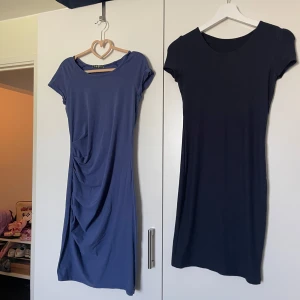 Två enkla kortärmade klänningar - Säljer två stilrena kortärmade klänningar i mjukt material. bomull Den ena är marinblå-lila med snygg drapering på sidan, den andra är svart och har en klassisk rak passform. Båda har rund halsringning och är knälånga, perfekta för dig som gillar minimalistisk stil.
