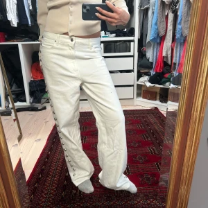 Vita wide jeans med pärlknappar H&M - Säljer ett par vita jeans från H&M med raka, wide ben och snygga pärlknappar längs hela yttersidan. Helt oanvända. Hög midja och klassisk femficksmodell. Materialet är kraftig bomull med jeanskänsla. Perfekta för dig som vill sticka ut med coola detaljer.