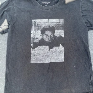 Svart t-shirt med tryck från OneWear - Svart t-shirt från OneWear i storlek XS med ett stort svartvitt tryck av en person på framsidan. Klassisk rund halsringning och korta ärmar. T-shirten är gjord i mjuk bomull och har en avslappnad vibe.