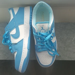 Nya blåvita sneakers med snörning - Snygga sneakers i blått och vitt med klassisk siluett och snörning. Storlek 37-38 !!Skorna har perforerad tå, rund tå och platt sula. Ovandelen är i syntetmaterial och de har en sportig vibe med tydliga blå detaljer och logga på plösen.