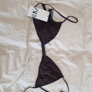 Mörkbrun bikiniöverdel från Zara - Snygg mörkbrun bikiniöverdel från Zara med trekantsformade kupor och smala axelband. Toppen har en cool detalj med svart spänne framtill och justerbara band för perfekt passform. Materialet är mjukt och stretchigt, perfekt för stranden eller poolen. Liten i storleken