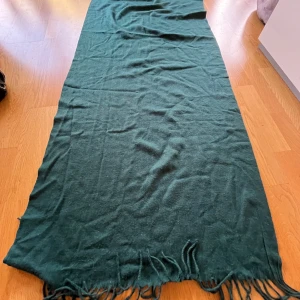 Mörkgrön halsduk med fransar - En stor och mjuk halsduk i mörkgrönt med långa fransar i kanterna. Perfekt att svepa runt halsen för extra värme. Halsduken är enfärgad och har en klassisk, tidlös look som funkar till de flesta outfits.          Säg till om du vill ha fler bilder🤗