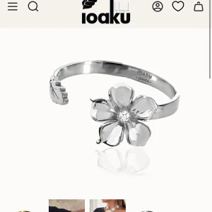 Silverfärgat La Fleur armband från Ioaku - Stilrent armband i silverfärg från Ioaku med en stor blomma i fokus och en gnistrande sten i mitten. Öppen design som gör det enkelt att ta på och av. Perfekt statement piece för dig som vill sticka ut med något unikt och trendigt. Helt oanvänd!! 