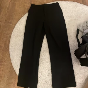Svarta kostymbyxor Gina Tricot 36 - Svarta kostymbyxor från Gina Tricot i storlek 36. Byxorna har raka ben, hög/normal midja och stängs med dragkedja, knapp och hake. Snygg och clean look som passar till många olika outfits. Materialet är mjukt och följsamt för en bekväm känsla. Har använts mycket och är riktigt älskade, men börjar tyvärr växa ur dem! Hör av er vid frågor och funderingar! 