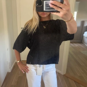 Svart blus med hålmönster - Svart blus med oversized passform och korta, vida ärmar. Blusen har ett genomgående hålmönster som ger en luftig känsla och en avslappnad look. Perfekt att styla med jeans eller kjol för en trendig vibe.