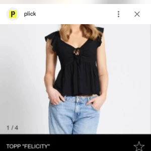 Svart blus med volangärm och knyt - Supersöt svart blus med volangärmar och v-ringning. Toppen har en knytning framtill och en luftig, lite utställd passform som ger en avslappnad vibe. Perfekt att styla med jeans eller kjol för en trendig look.