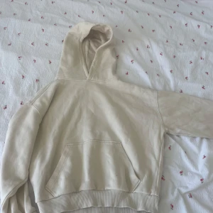 Beige hoodie med huva och ficka - Säljer en beige hoodie från C i storlek 134/140. Tröjan har en stor huva och en klassisk magficka framtill. Mjuk insida och ribbade muddar vid ärmslut och nederkant. Perfekt för chill dagar och enkel att matcha med jeans eller mjukis.