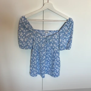 Blommig blå blus från Bubbleroom XS - Supersöt blå blus från Bubbleroom i storlek XS med vita blommor, puffiga korta ärmar och smockad struktur. Aldrig använd, som ny.