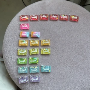 Färgglada glittriga berlocker Sweet - Säljer ett gäng söta berlocker i olika färger med texten 'Sweet' på. De är rektangulära och har glittriga detaljer i resin, perfekta att använda till halsband, armband eller örhängen. Färgerna är blandade: röd, rosa, gul, grön, blå, lila och orange. Supergulliga och unika accessoarer!