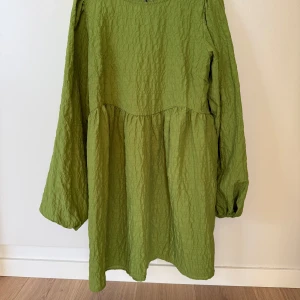 Envii grön långärmad klänning, storlek M - Jättefin olivgrön klänning från Envii med långa ärmar och en avslappnad passform. Klänningen har en rund halsringning och knytning på baksidan upptill. I nästintill oanvänt skick- endast använd två gånger och säljes pga att den blivit för stor.