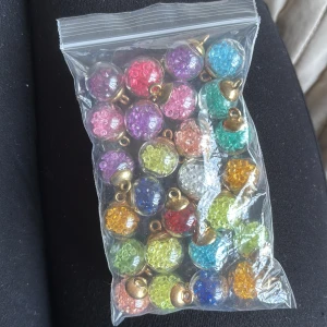 Färgglada glittriga berlocker till smycken - Säljer ett gäng runda berlocker i transparent plast med glittriga pärlor inuti. Finns i flera färger som rosa, blå, grön, gul, lila och röd, med guldfärgade detaljer upptill. Perfekt för att göra egna halsband, armband eller örhängen. Superfina att mixa och matcha för en personlig stil!