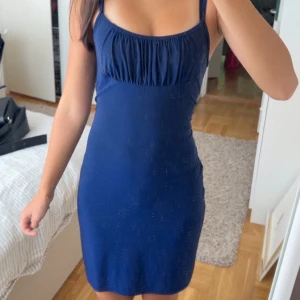 Marinblå kortklänning från Pipeline - Snygg marinblå klänning från Pipeline i kort modell med smala axelband och rynkad detalj vid bysten. Klänningen har en figurnära passform och är tillverkad i mjukt, stretchigt material som sitter bekvämt. Perfekt för dig som gillar stilrena och enkla plagg med en twist.