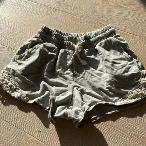 Grå shorts med spets från Lindex - Snygga grå shorts från Lindex med elastisk midja och snörning framtill. De har dekorativ spets i vitt på sidorna och är gjorda i mjuk bomull. Perfekta för chill dagar och sommarhäng. Passar dig som gillar bekvämt och stilrent.